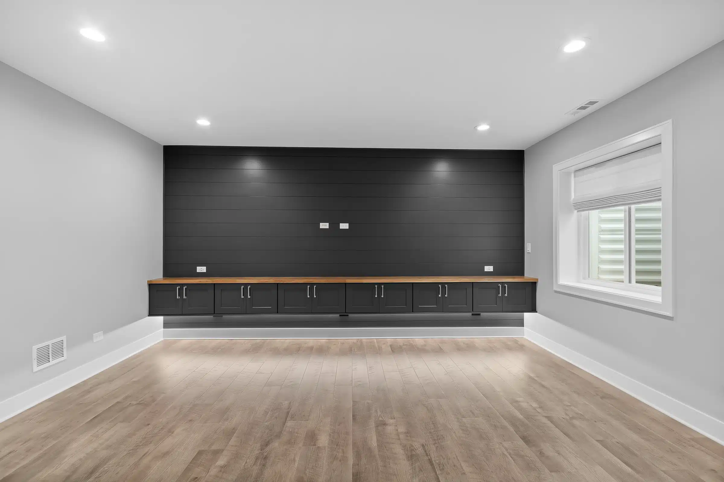 Custom basement entertainment wall featuring charcoal shiplap, floating black cabinets with a wood countertop, and LED accent lighting in Palatine.
