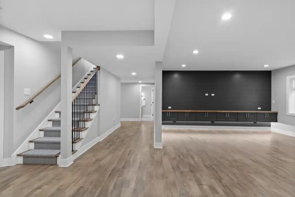 Finished basement layout in Palatine showing open staircase with carpet runner, luxury vinyl plank flooring, and a black shiplap entertainment wall.