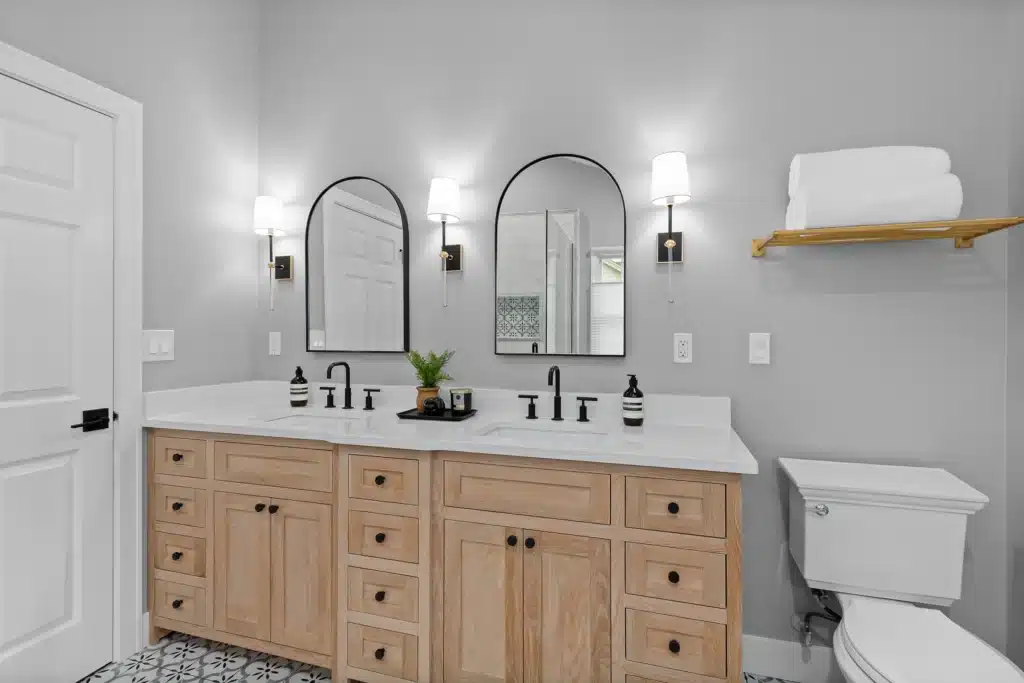 Modern bathroom renovation in Palatine featuring a natural light oak double vanity, matte black arched mirrors, and geometric floor tile.