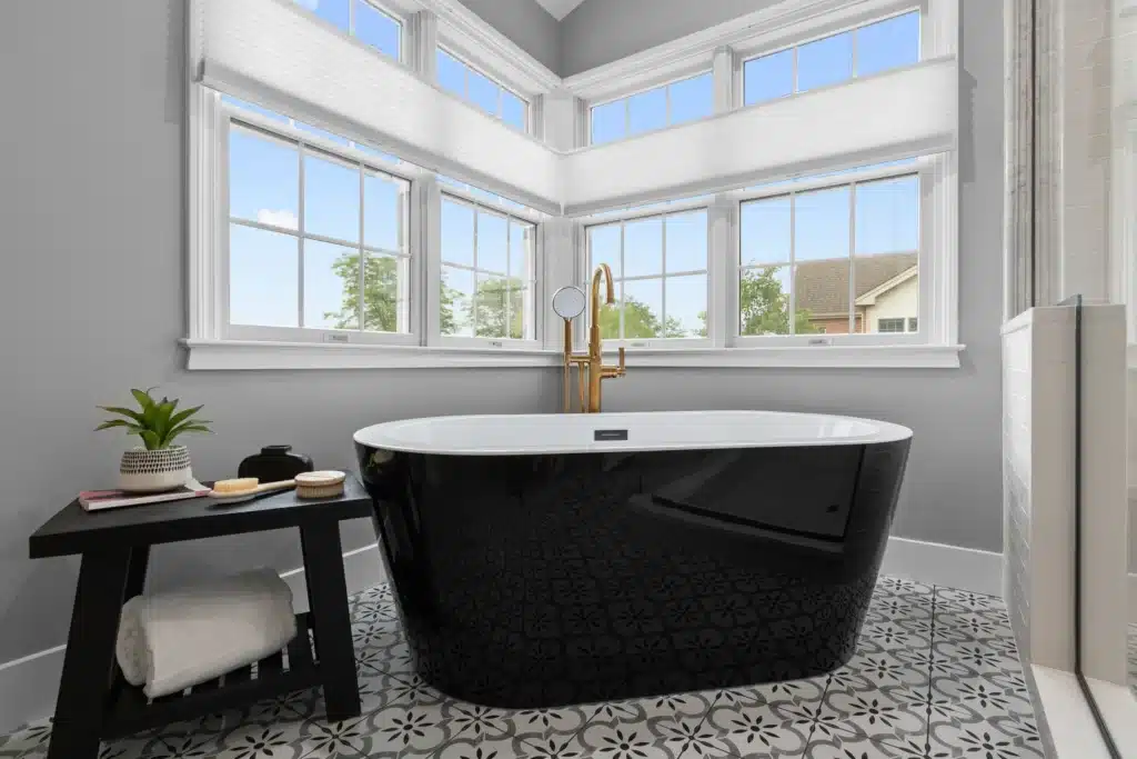 Modern black freestanding soaking tub in a Palatine master bath, featuring black and white patterned floor tile, brushed gold tub filler, and wrap-around corner windows.