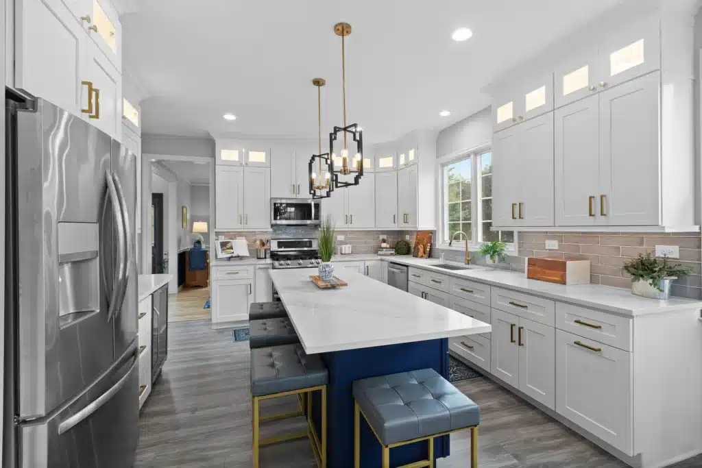 Transitional kitchen renovation in Palatine featuring white shaker cabinets, a navy blue island with quartz countertops, and geometric gold pendant lighting.