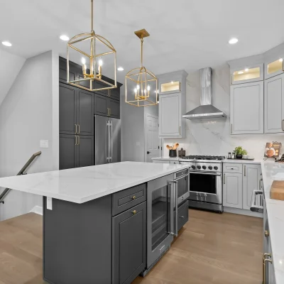 Modern kitchen renovation in Palatine featuring a charcoal grey island with a built-in wine fridge, white quartz countertops, and gold cage pendant lighting.