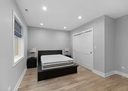 Modern basement guest bedroom suite with large egress window, gray walls, and luxury vinyl plank flooring in Palatine renovation.