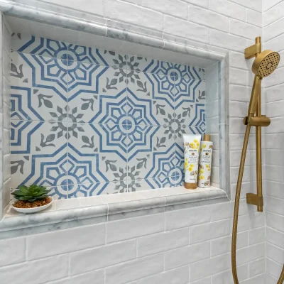 Close up of a custom shower niche featuring blue and white patterned encaustic tile, marble trim, and brushed gold shower fixtures in Palatine.