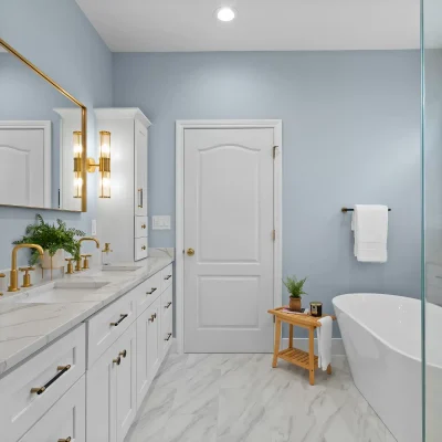 Luxury master bathroom renovation in Palatine featuring a white double vanity with brushed gold hardware, a large gold-framed mirror, and marble-look porcelain flooring.