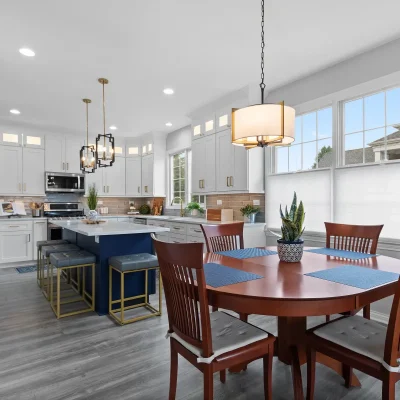 Open concept kitchen renovation in Palatine featuring white cabinets, a navy blue island with gold stools, and a bright adjacent dining area with large windows.