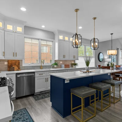 Open concept kitchen remodel in Palatine connecting to a vaulted ceiling family room, featuring a navy island, pendant lighting, and grey luxury vinyl plank flooring.