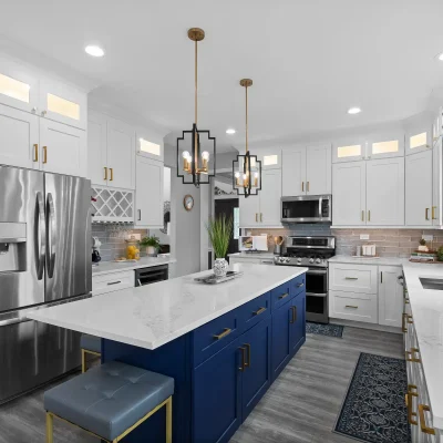 Close up of white quartz kitchen countertops with grey veining on a navy blue island. Features include gold drawer pulls, a stainless steel fridge, and a built-in wine rack.